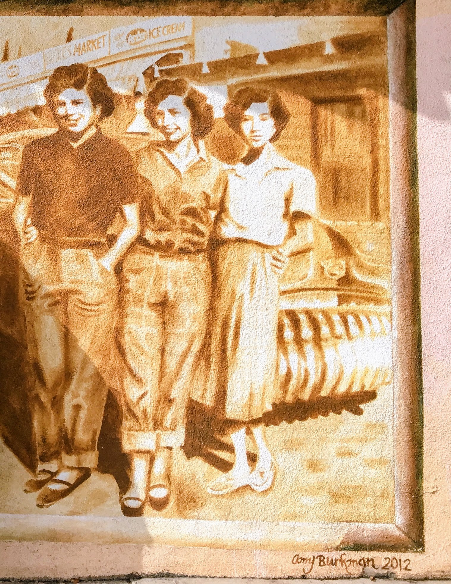 Sepia mural of three women posing in vintage attire, with a retro car and market signs in the background.