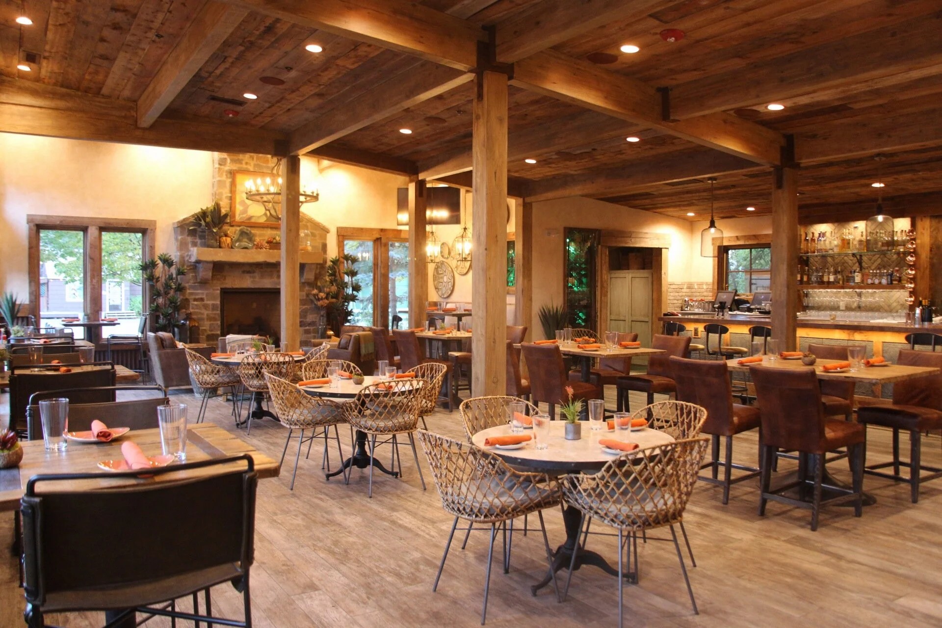 Cozy restaurant interior with wooden decor and round tables set with orange napkins.