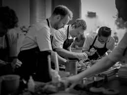 Chefs focused on food preparation in a kitchen, wearing aprons and working together.