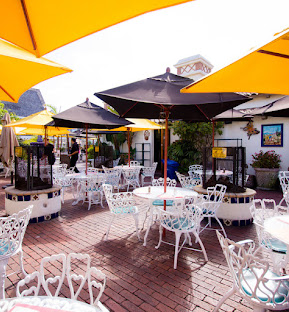Outdoor cafe with white chairs, brick floor, and yellow umbrellas.