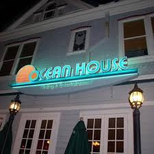 Neon-lit sign reading 'Ocean House' on building exterior at night.