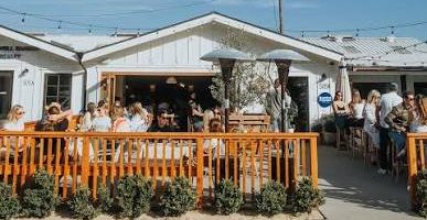 Crowded outdoor patio at a cafe with string lights under a blue sky.
