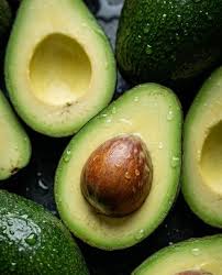Halved avocados, some with seeds, on a dark surface with water droplets.
