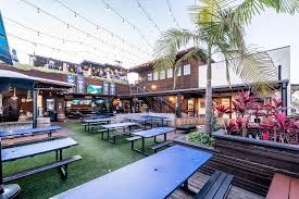 Outdoor seating area with picnic tables, palm trees, and string lights.