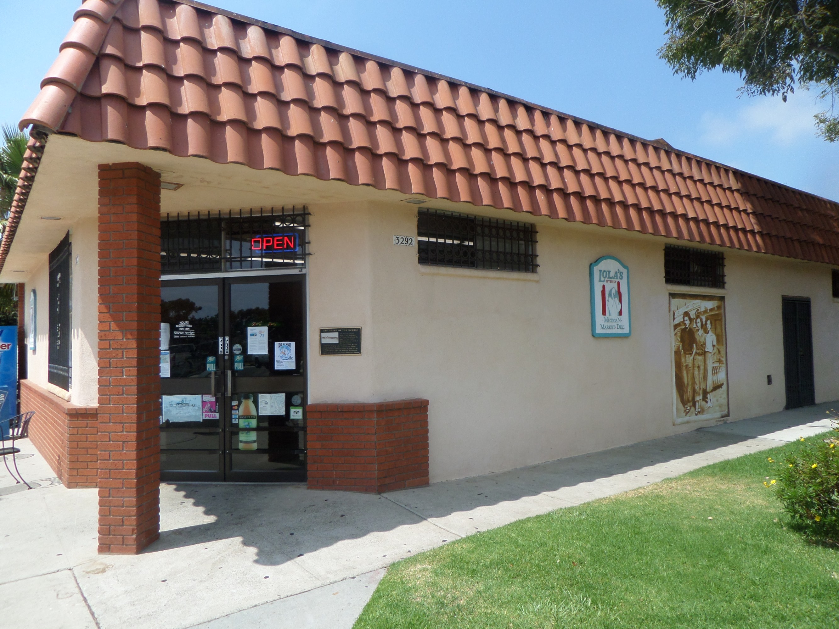 Small building with red tiled roof, brick pillars, glass door displaying an open sign.