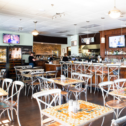 Empty restaurant with patterned tables, bar, and TV screens on the walls.