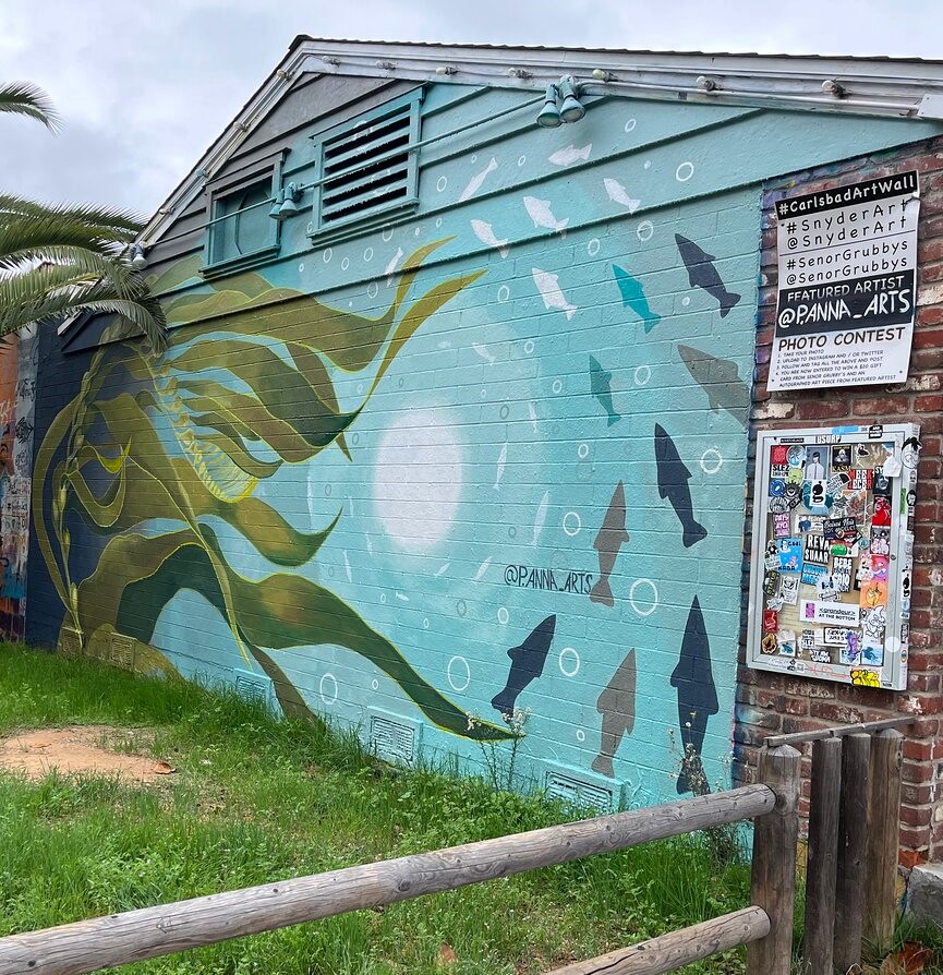 Mural of a sea turtle and fish on a building wall with a contest notice.