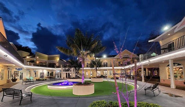 Courtyard with purple lights and palm tree at dusk, surrounded by buildings.