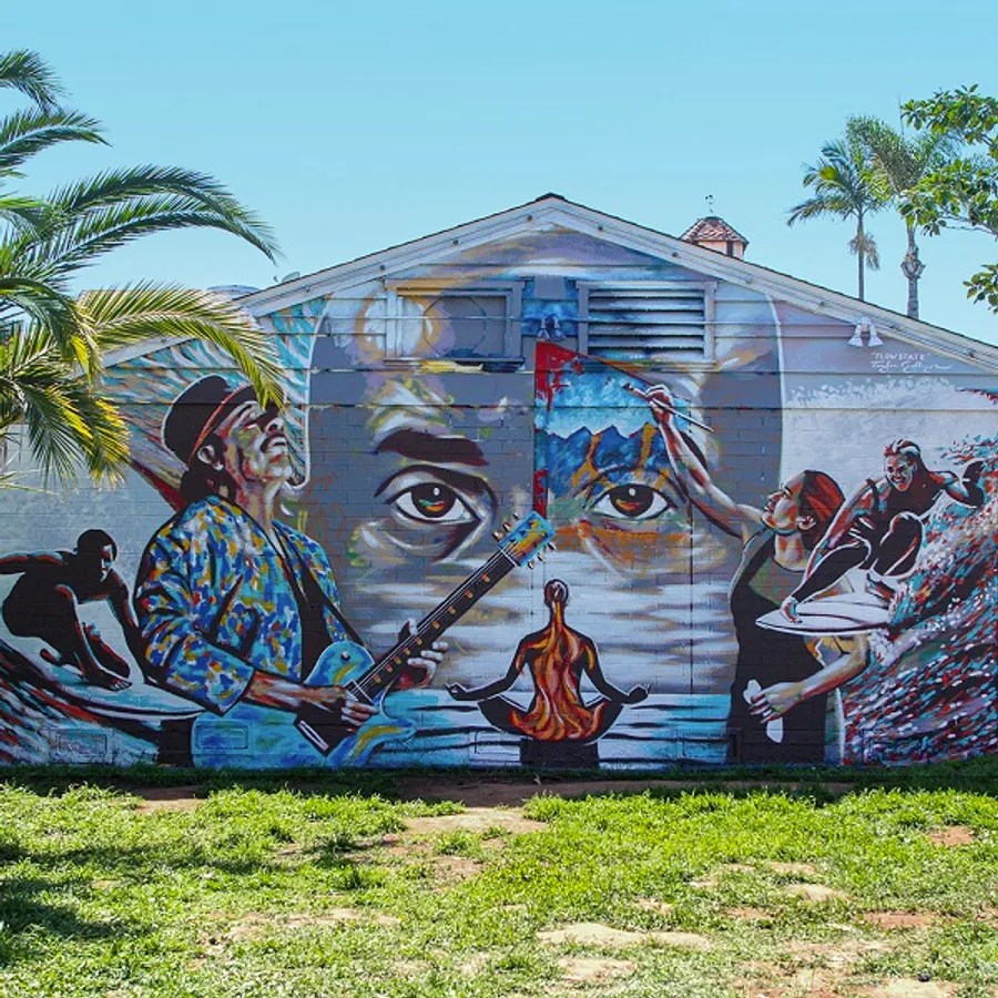 Colorful mural with musicians, surfer, and meditating figure on a building wall under palm trees.