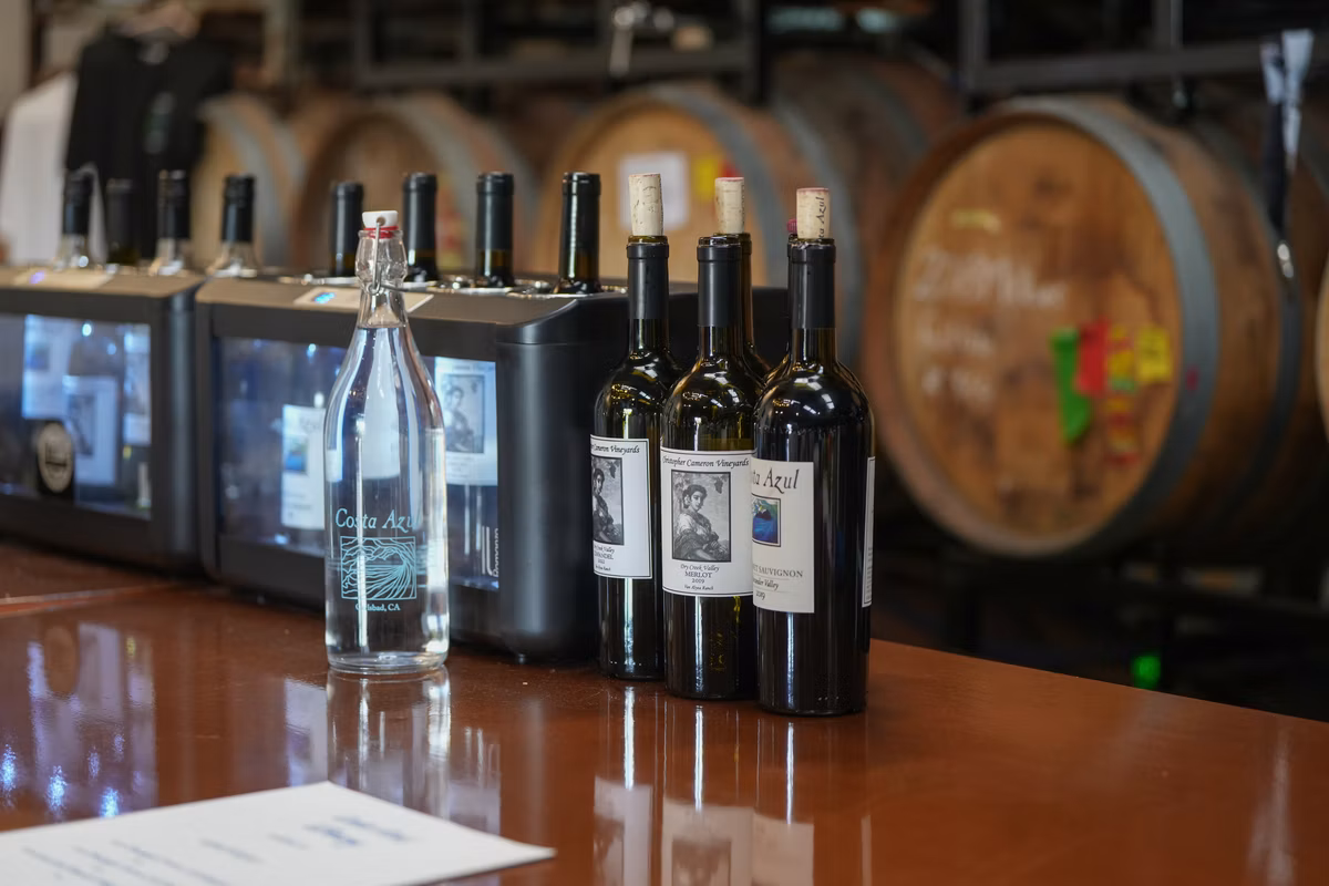 Wine bottles and water on bar counter with barrels in background.