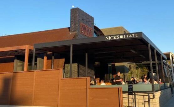 Outdoor diners at a restaurant named 'Nick's' during sunset.