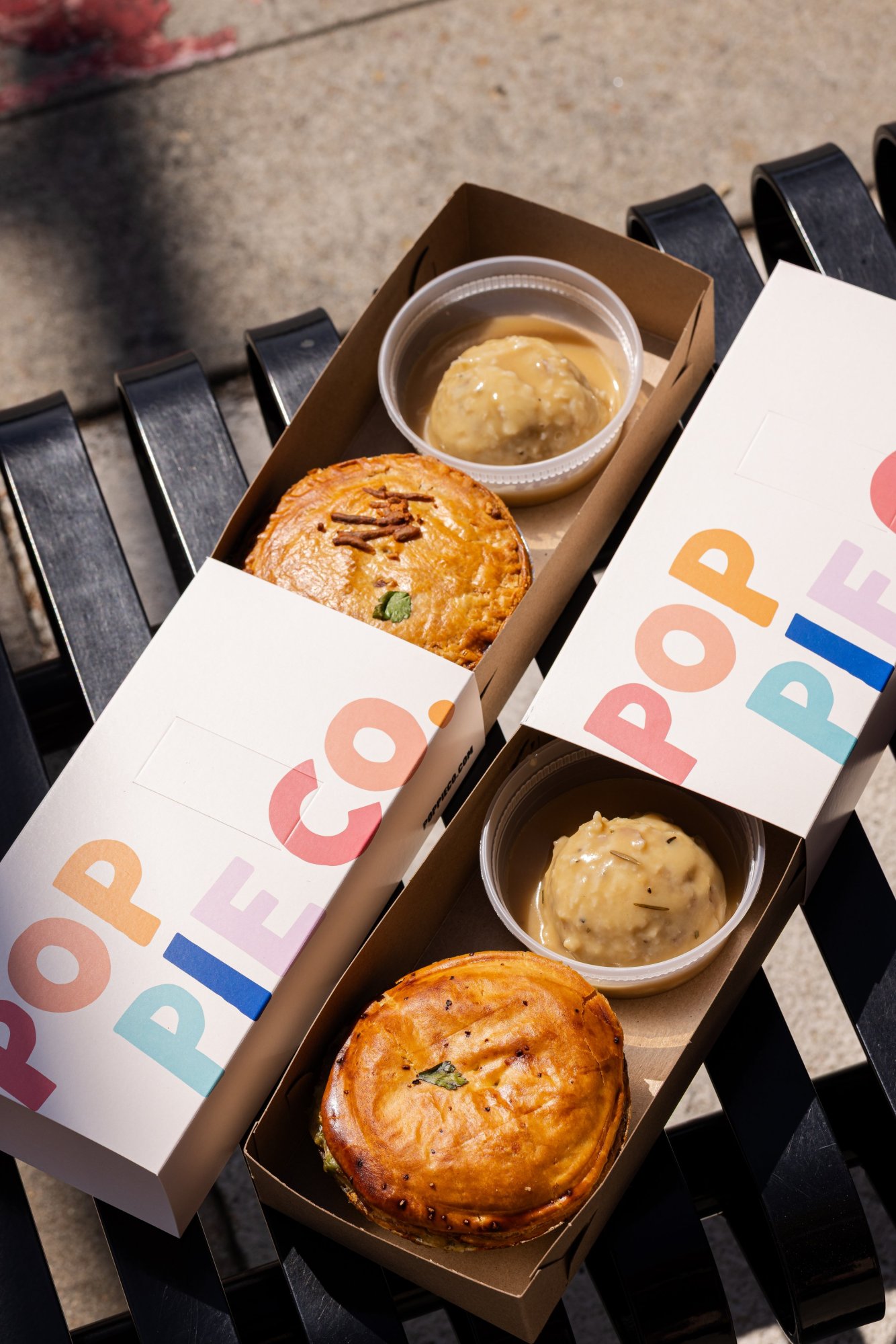 Two boxed pies with gravy on a bench.