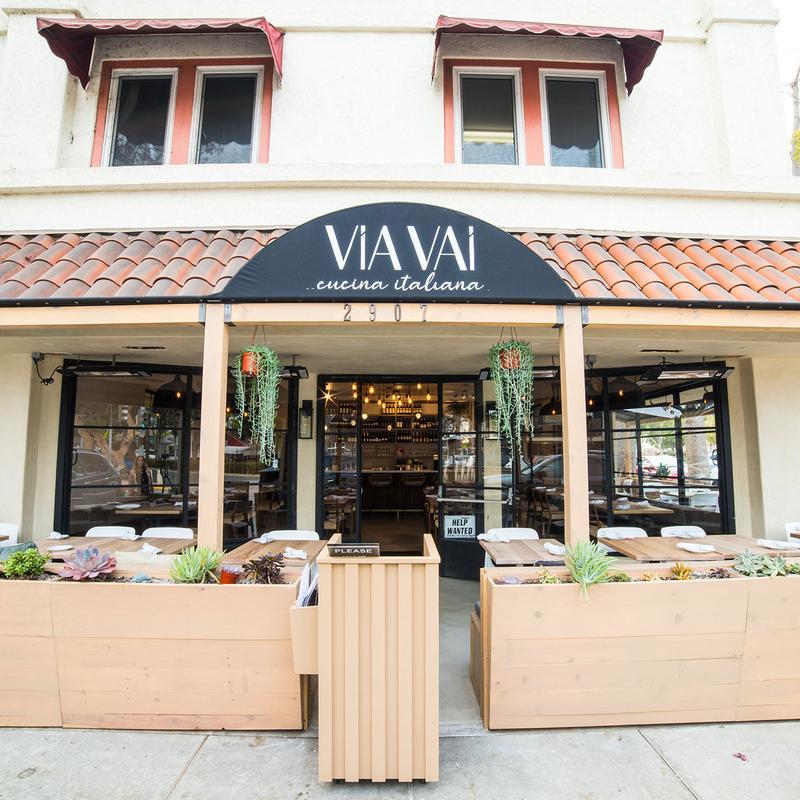 Italian restaurant facade with outdoor seating and hanging plants.