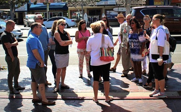 Group of people standing and chatting on a sunny sidewalk.