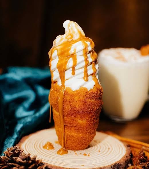Ice cream cone topped with caramel sauce on wooden base.