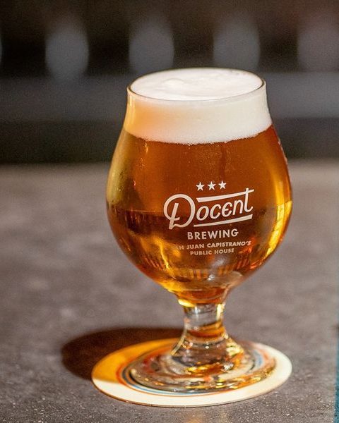 Glass of beer next to a brewing batch card on a table.