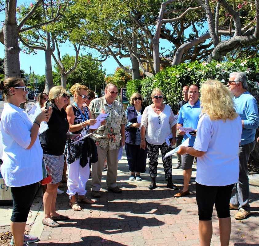 A group of people gathered outdoors, listening to a woman speak.